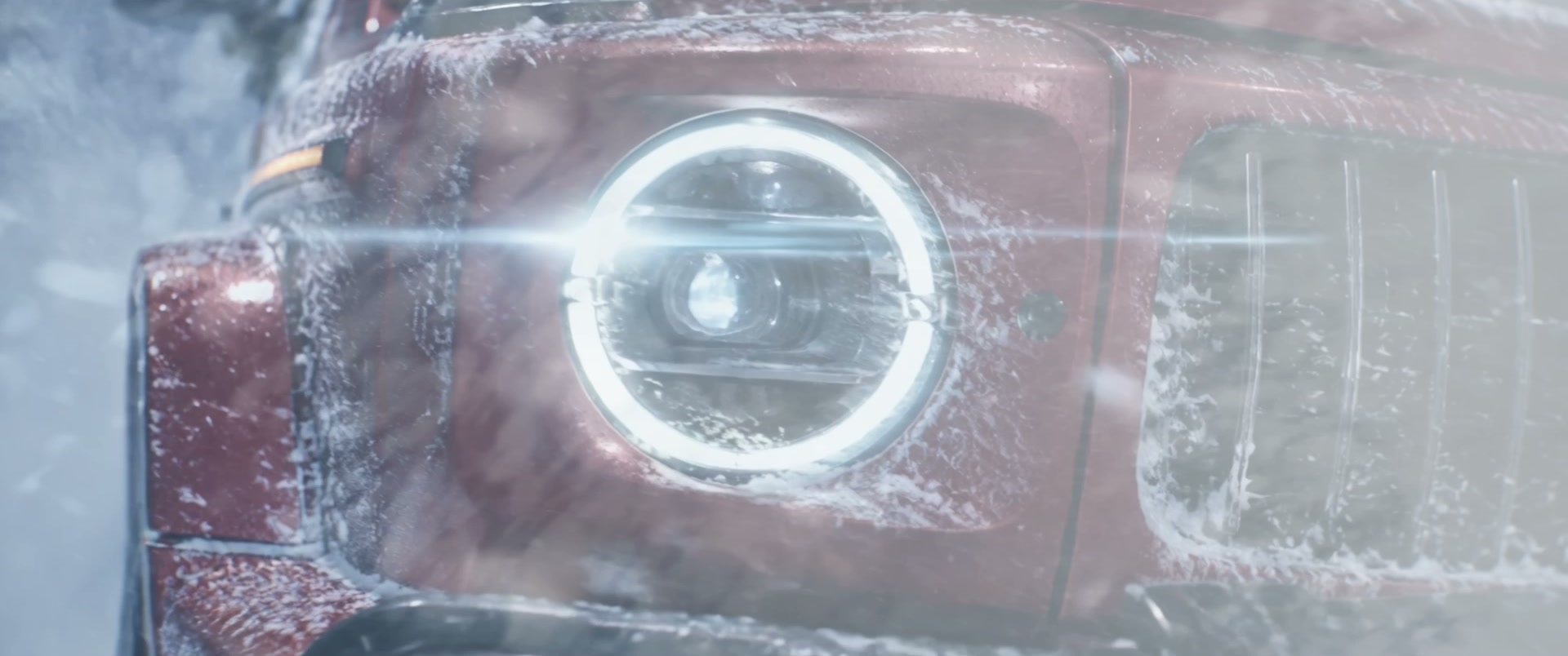 Close-up of the G-Class headlight and burgundy grille covered in snow